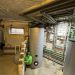Kellerraum mit großem Pufferspeicher, Rohrleitungen und Bosch Inneneinheit an Wand.