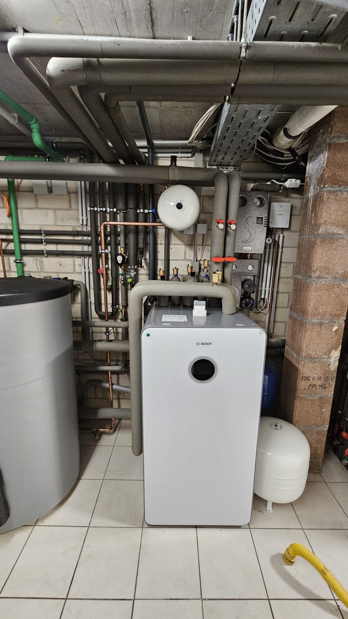 Bosch-Wärmepumpen-Inneneinheit mit umfangreicher Verrohrung und Speichertank in einem gut ausgestatteten Heizungsraum installiert.