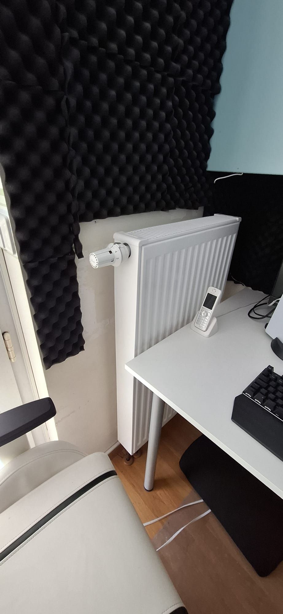 Heizkörper mit Thermostat unter Schreibtisch im Büro, umgeben von schwarzem Schallschutzschaum.