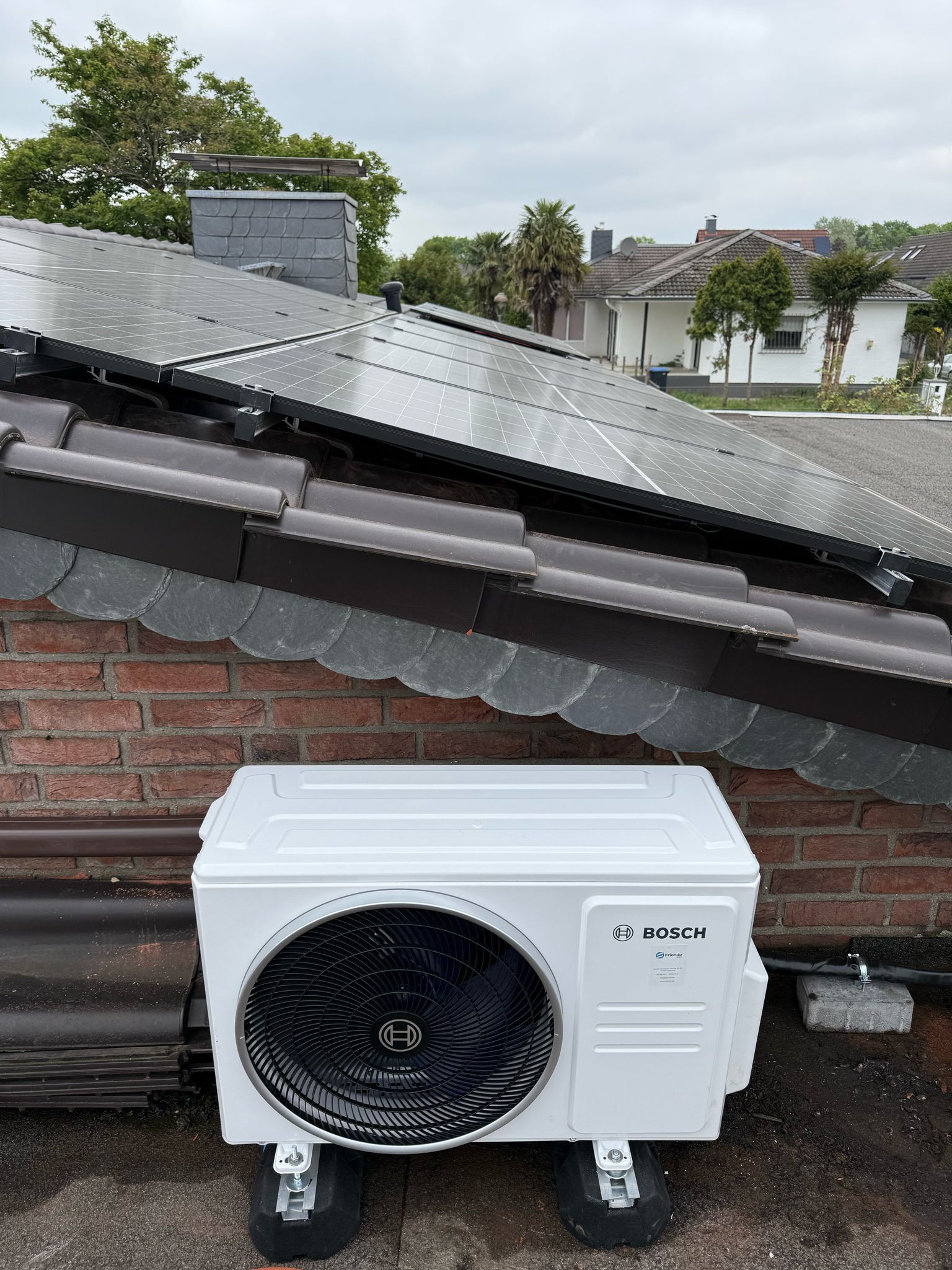 Bosch Klima Außengerät auf Flachdach, davor geneigte Solarmodule auf Ziegeldach.