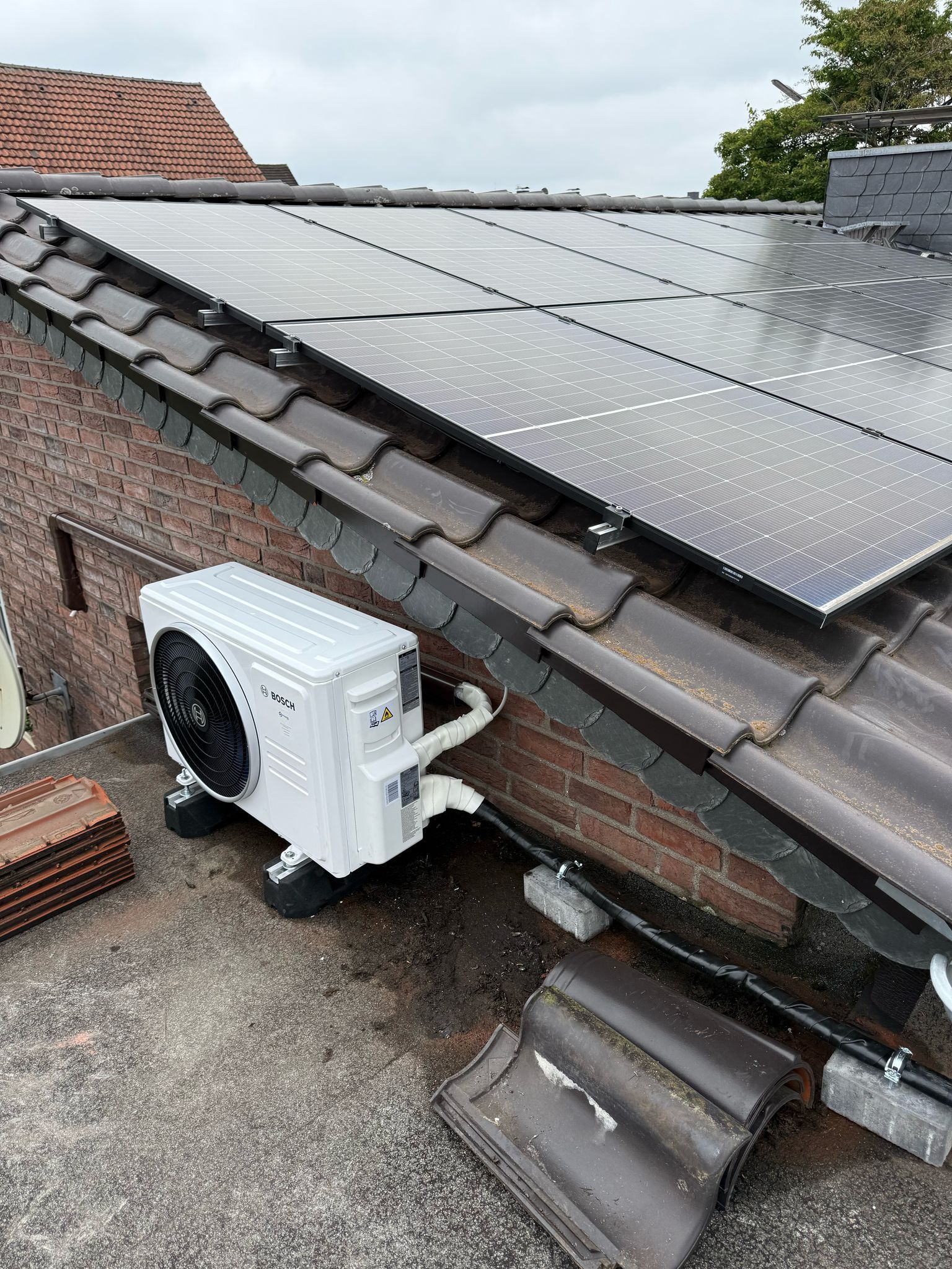 Außeneinheit der Bosch Klimaanlage neben Hauswand, angeschlossen unter Solarmodulen.