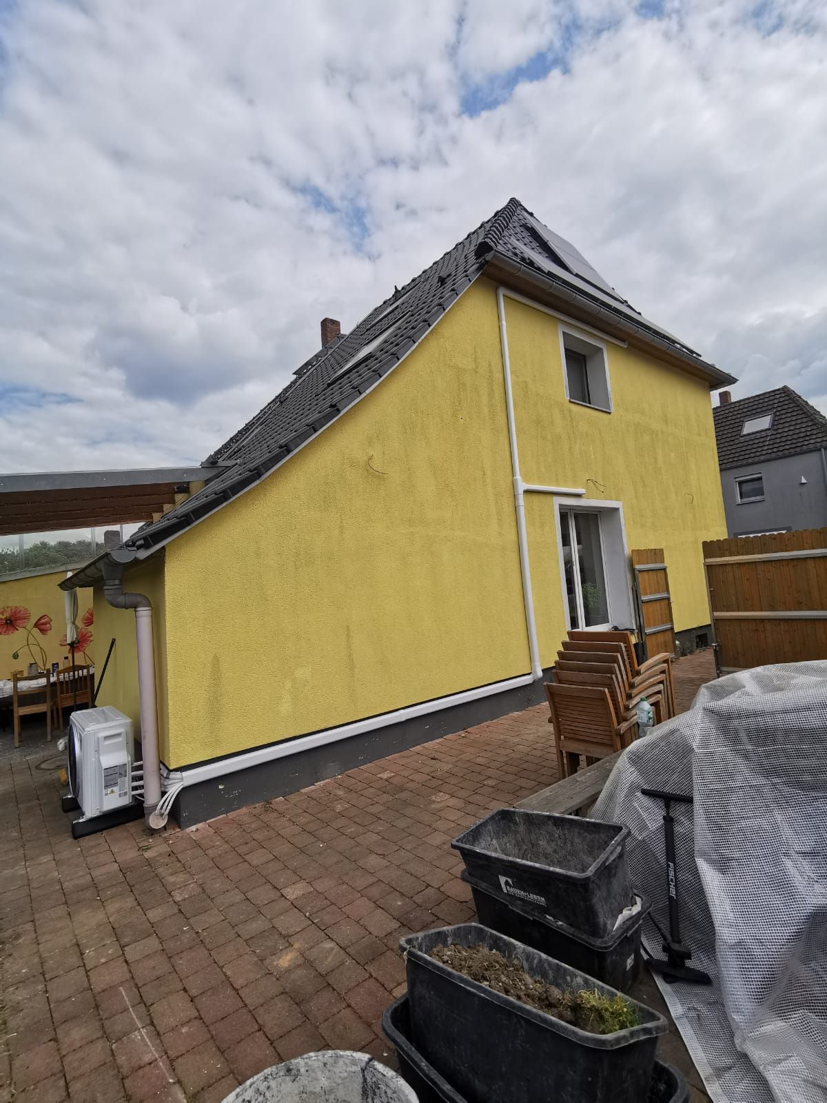 Gesamtansicht eines gelben Wohnhauses mit installiertem Multisplit-Außengerät, Terrasse und gepflasterter Hof.