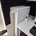 Heizkörper mit Thermostat unter Schreibtisch im Büro, umgeben von schwarzem Schallschutzschaum.