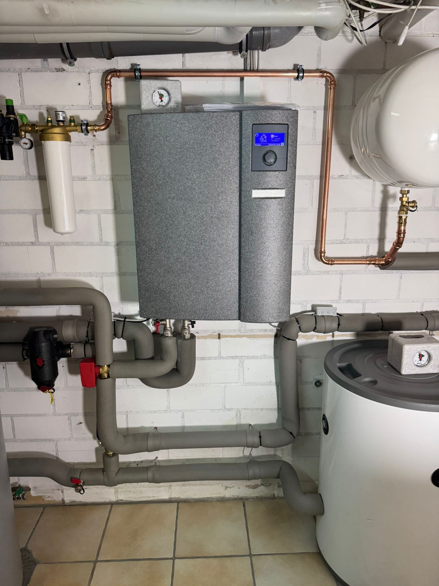 Detail der Heizungssteuerung mit Anzeige, Kupferleitungen und isolierten Rohranschlüssen.