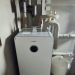 Wärmepumpen-Inneneinheit mit Pufferspeicher in grauem Technikraum, isolierte Rohre verlaufen an Wand und Decke.