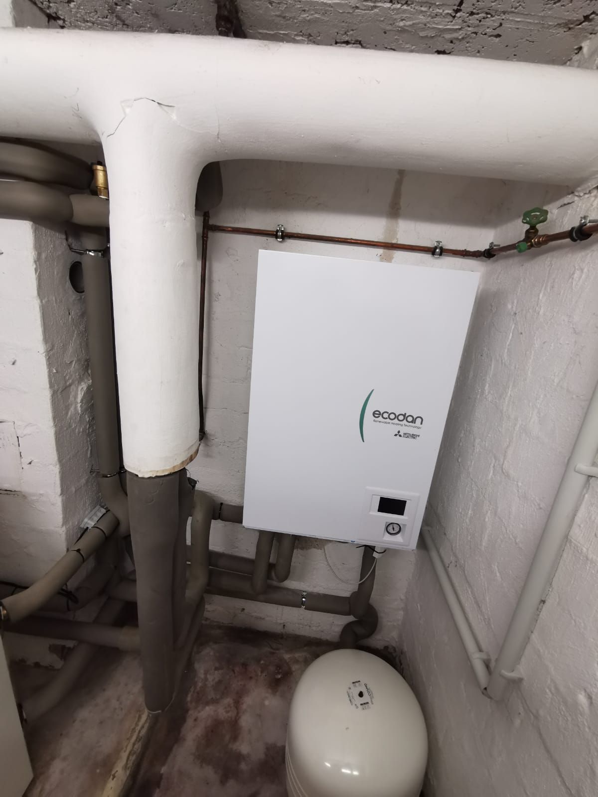 Wandmontierte Ecodan Steuerung im Keller neben Ausdehnungsgefäß und Rohrleitungen.