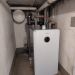 Bosch-Heizungseinheit in engem Kellerraum mit vielen isolierten Rohrleitungen und Wandarmaturen.