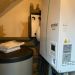 Ecodan-Wärmepumpenmodul an Wand mit Pufferspeicher, Isolierungen und aufliegenden Bedienungsanleitungen.