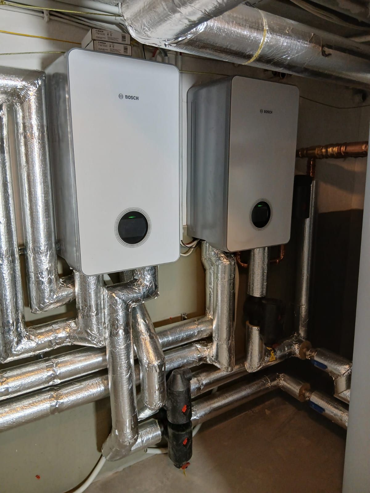 Zwei Bosch Steuergeräte an Kellerwand, angeschlossen an isolierte Rohrleitungen.