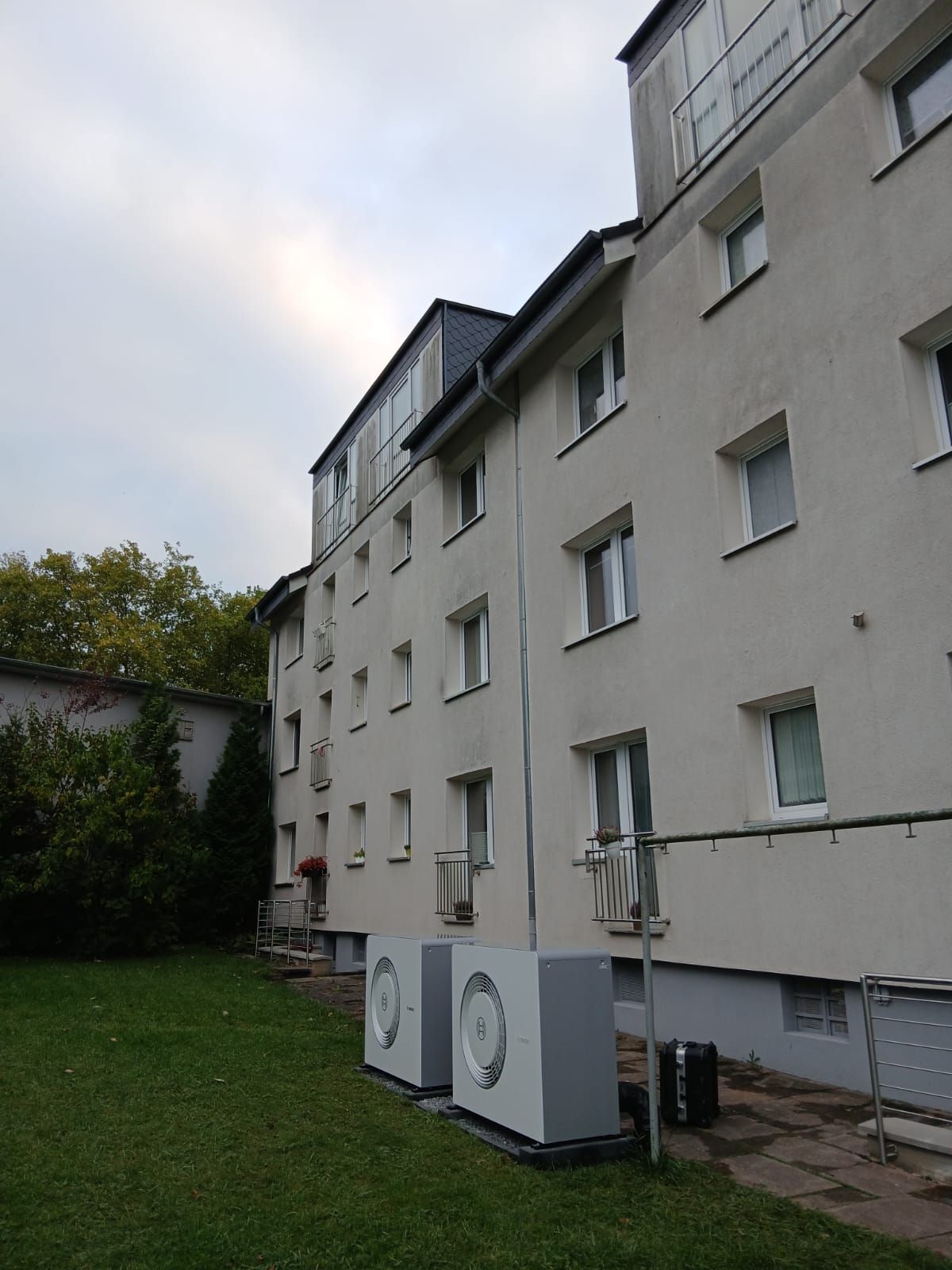 Mehrfamilienhaus Außenansicht mit zwei Bosch Wärmepumpen Außeneinheiten auf Rasenfläche.