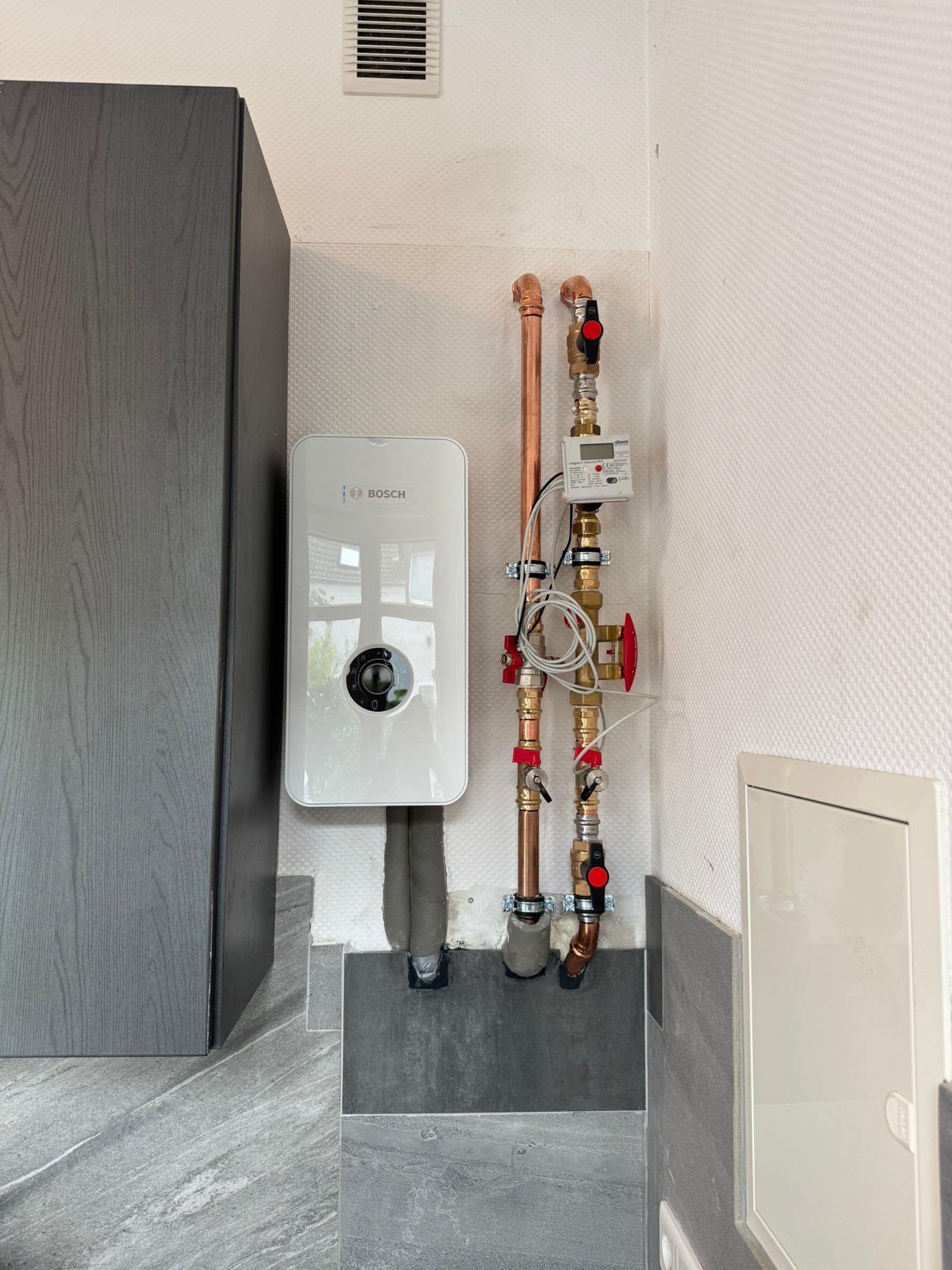 Bosch Durchlauferhitzer oder Steuergerät an Innenwand mit sichtbaren Wasserleitungen.