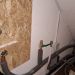Wasseranschlüsse mit Isolierung und Absperrhähnen unter Treppe an weißer Wand mit Holzverkleidung.