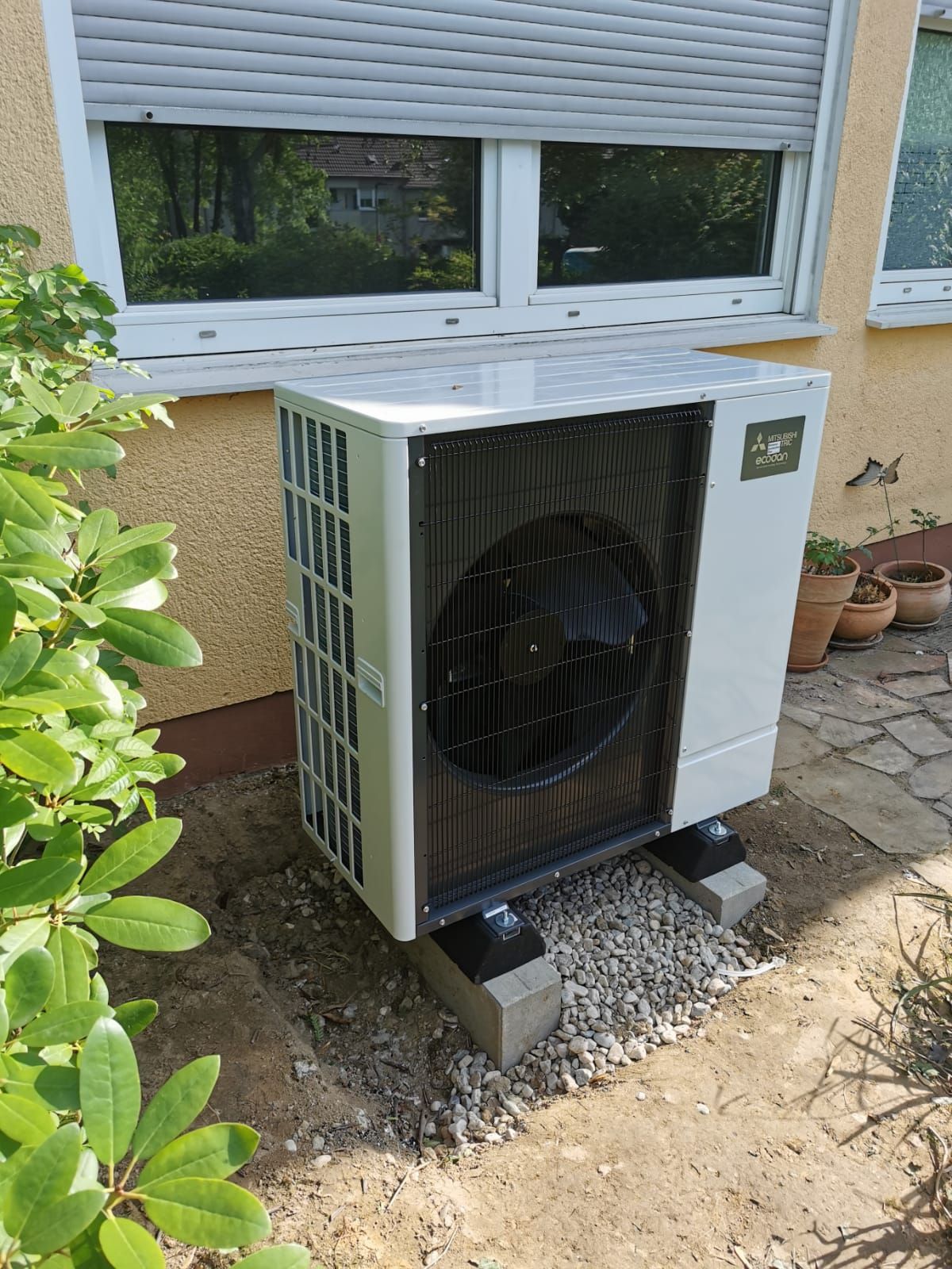 Mitsubishi Ecodan Wärmepumpen Außeneinheit auf Betonfundament vor Hauswand unter Fenster.
