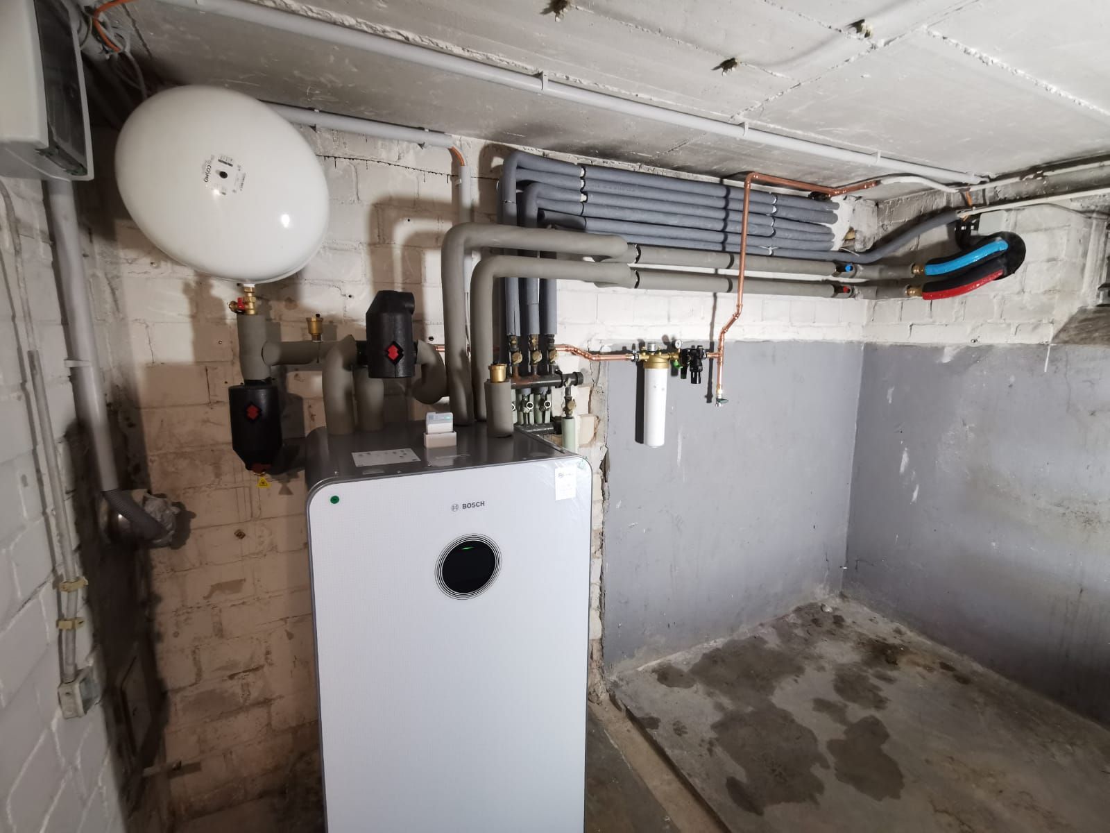 Bosch-Heizung im Keller mit isolierten Leitungen, Expansionsgefäß und freiliegender Ziegelwand.
