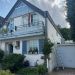 Weißes Einfamilienhaus mit Dachgaube, Balkon, Garten und Garage, Leiter an der Seitenwand angelehnt.
