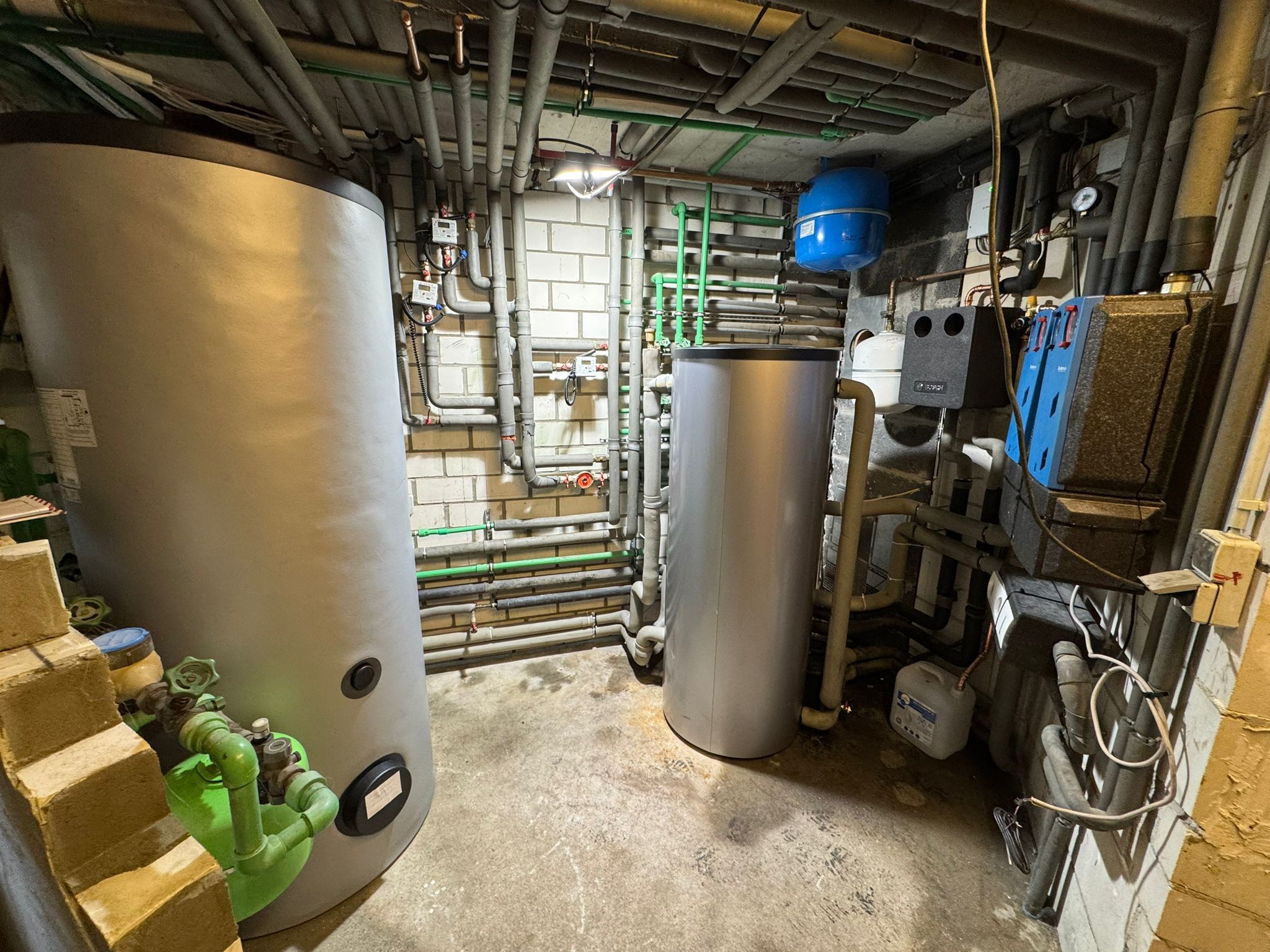 Technikraum mit zwei stehenden Speichern, gedämmten Leitungen und Verteilerrohren.