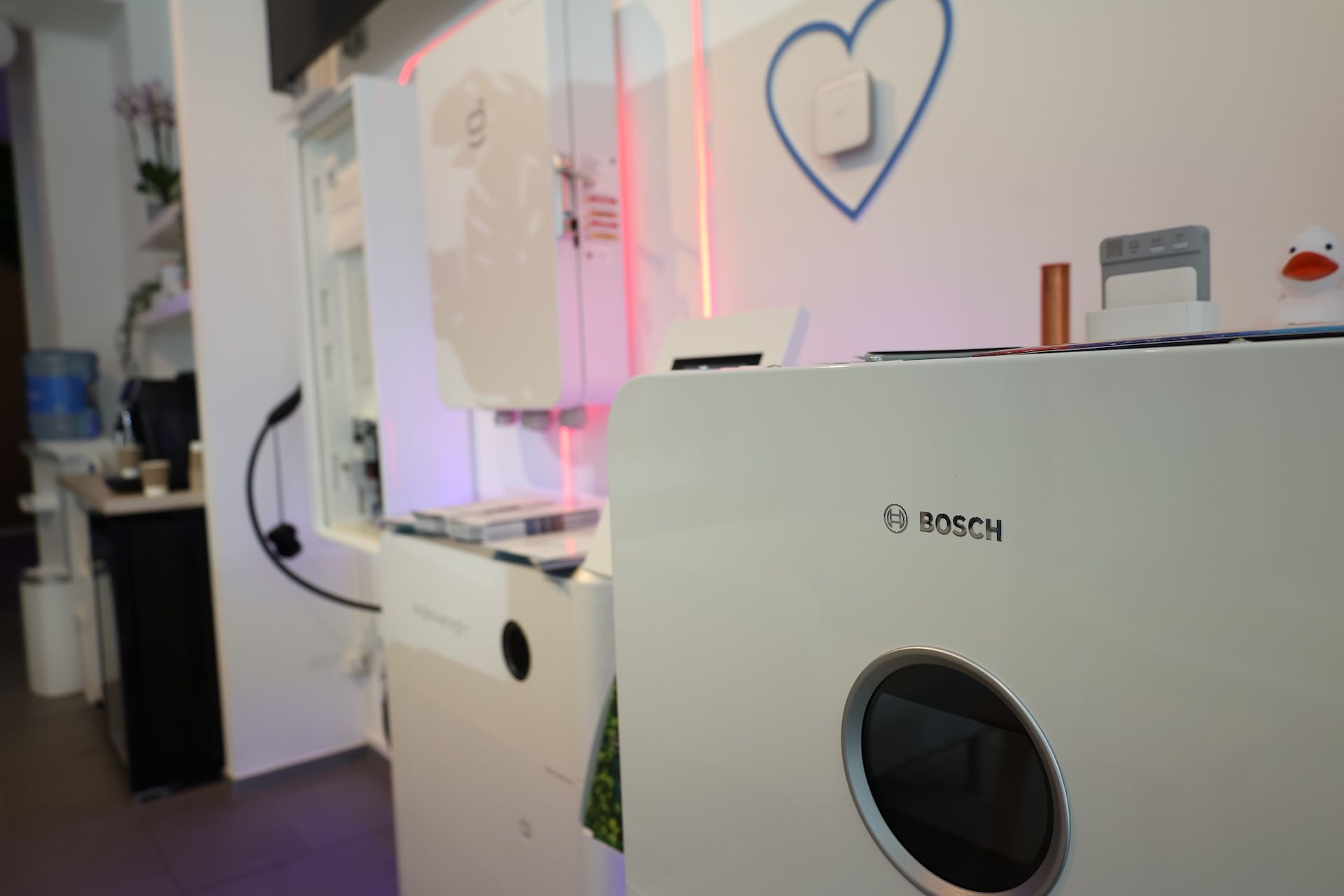Techniker montiert Außeneinheit einer Bosch-Wärmepumpe an einer Hauswand, Werkzeugtasche auf dem Rasen davor.