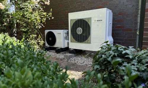 Bosch Außeneinheiten der Klimaanlage im Gartenbereich, umgeben von Sträuchern vor Hauswand.