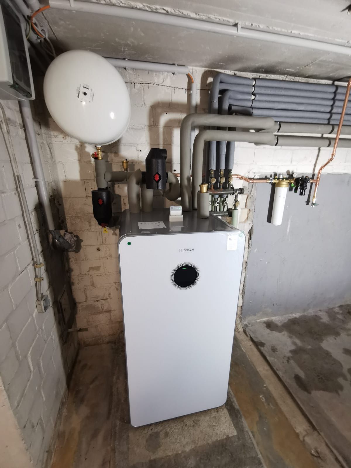 Bosch-Heizung im Keller mit isolierten Leitungen, Expansionsgefäß und freiliegender Ziegelwand.