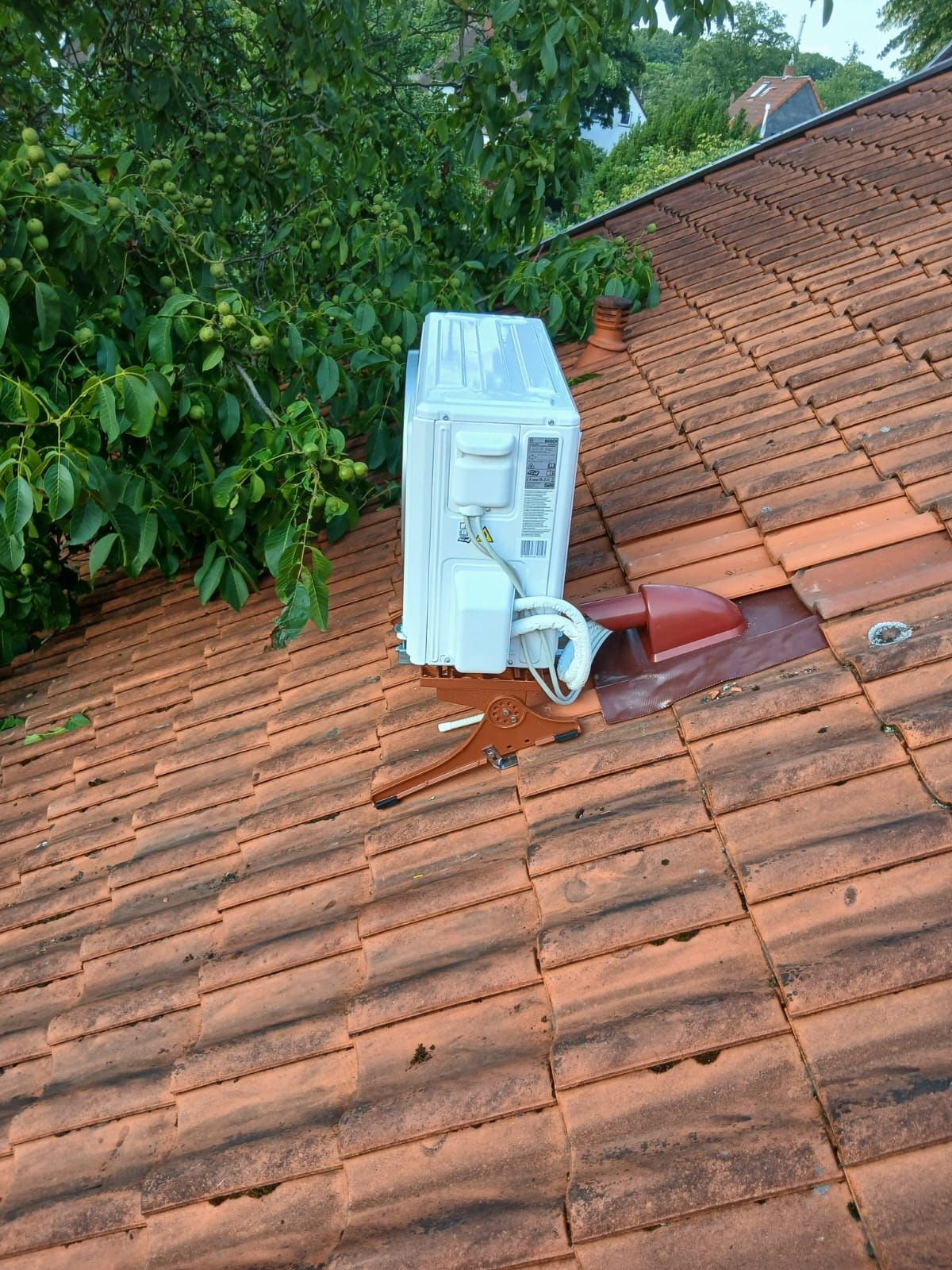 Bosch Klima Außeneinheit auf Ziegeldach montiert, befestigt auf Dachhalterung nahe Baumkrone.