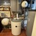 Technikraum mit Pufferspeicher, Wandgerät, zwei Ausdehnungsgefäßen und zahlreichen Rohrverbindungen.
