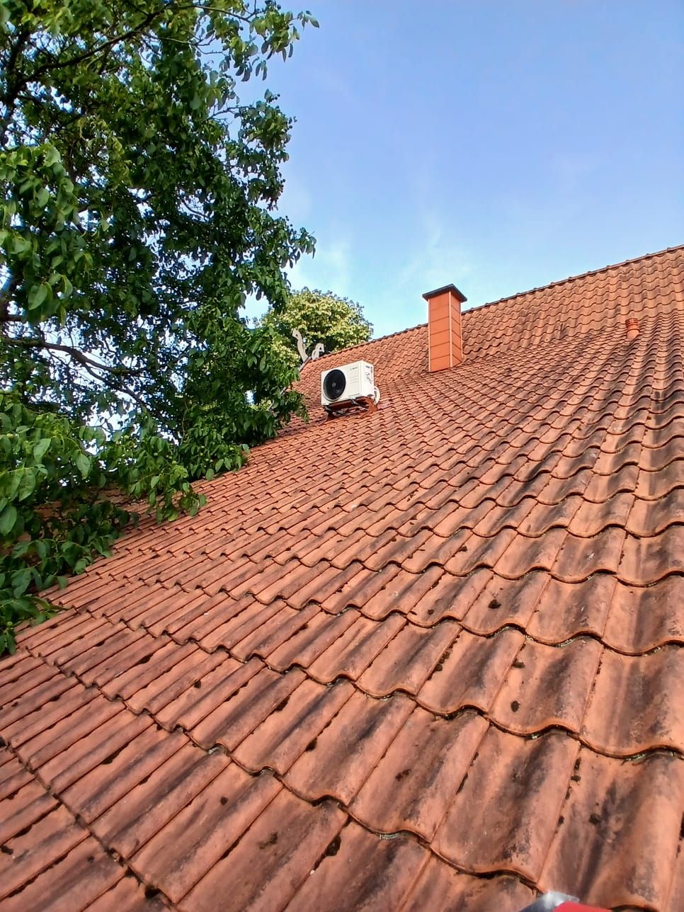 Bosch Außengerät auf geneigtem Ziegeldach, installiert oberhalb der Dachfläche nahe Schornstein.