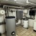 Kellerraum mit Wärmepumpe, Pufferspeicher und Heizungsrohren unter niedriger Decke.