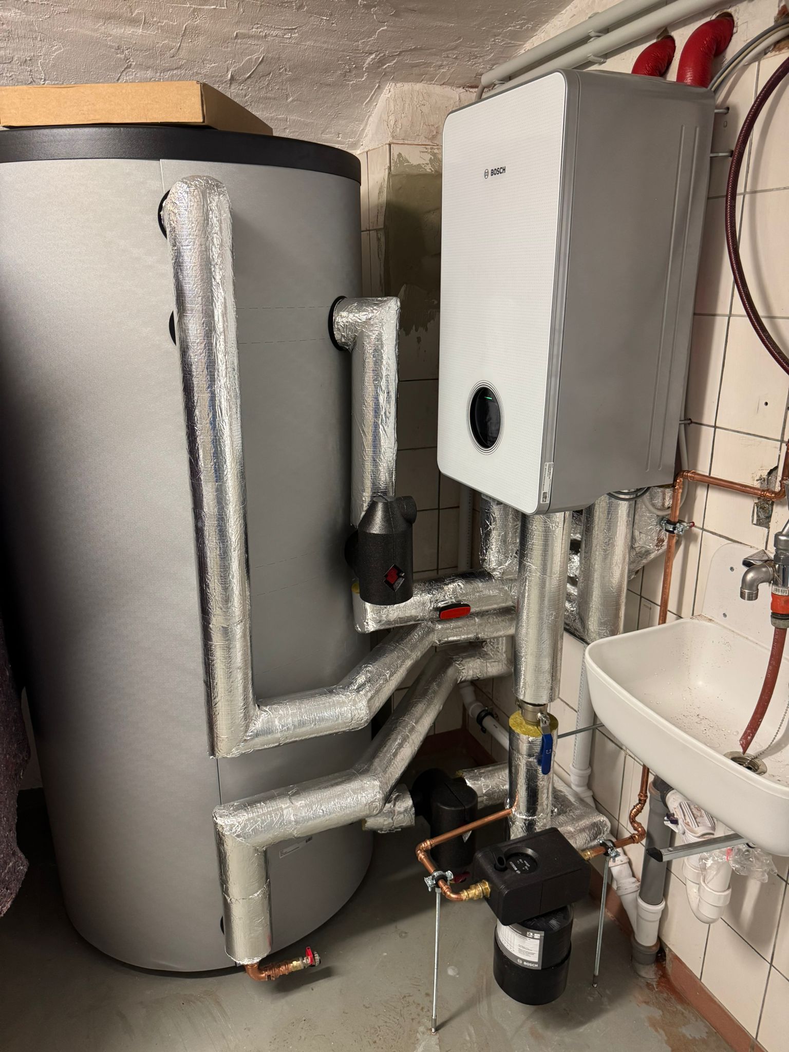 Bosch Wärmepumpen Inneneinheit mit Pufferspeicher und isolierten Rohrleitungen im Kellerraum.