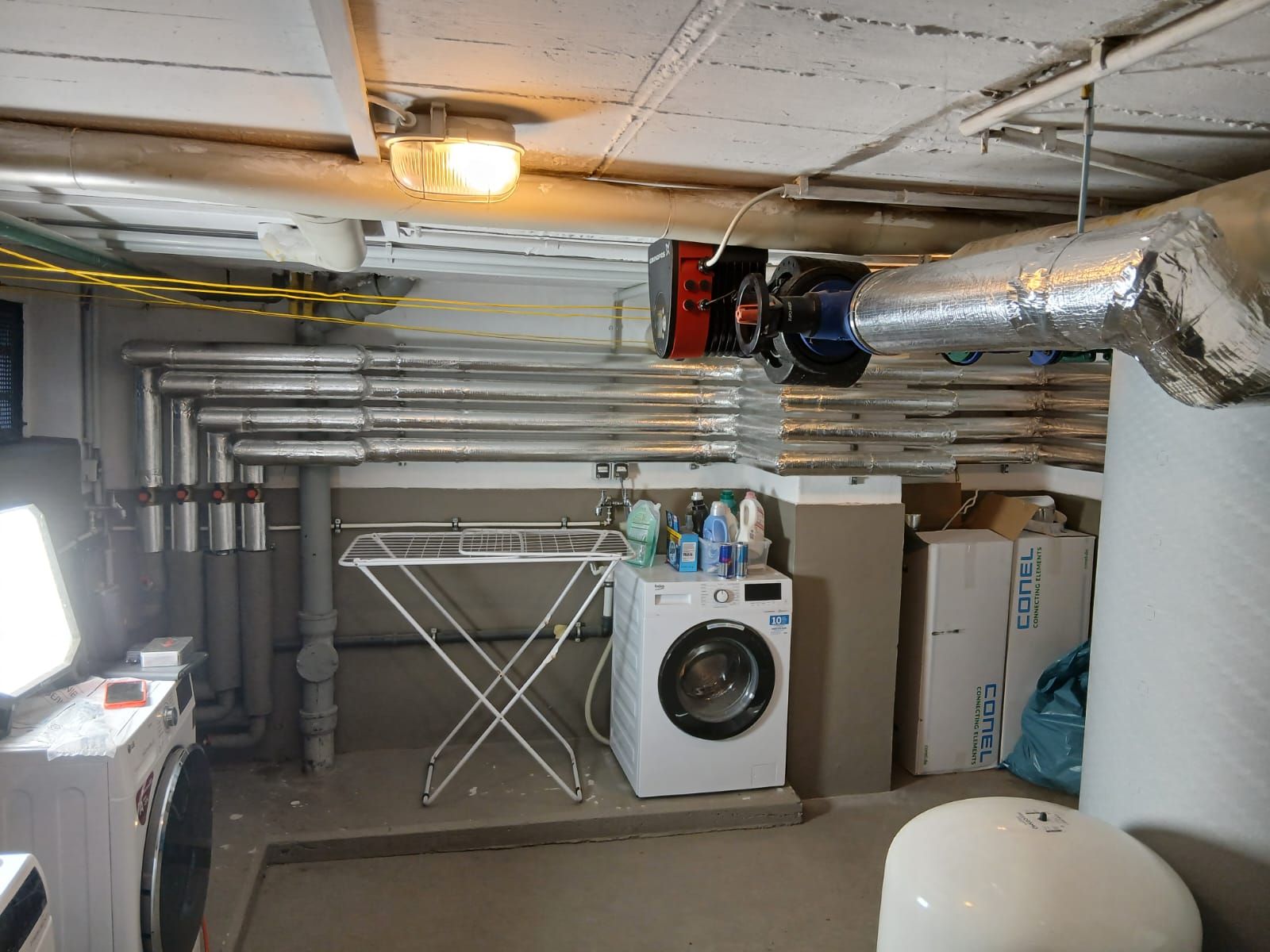 Kellerraum mit Heizungsrohren, Umwälzpumpe, Waschmaschine und Technikinstallation.