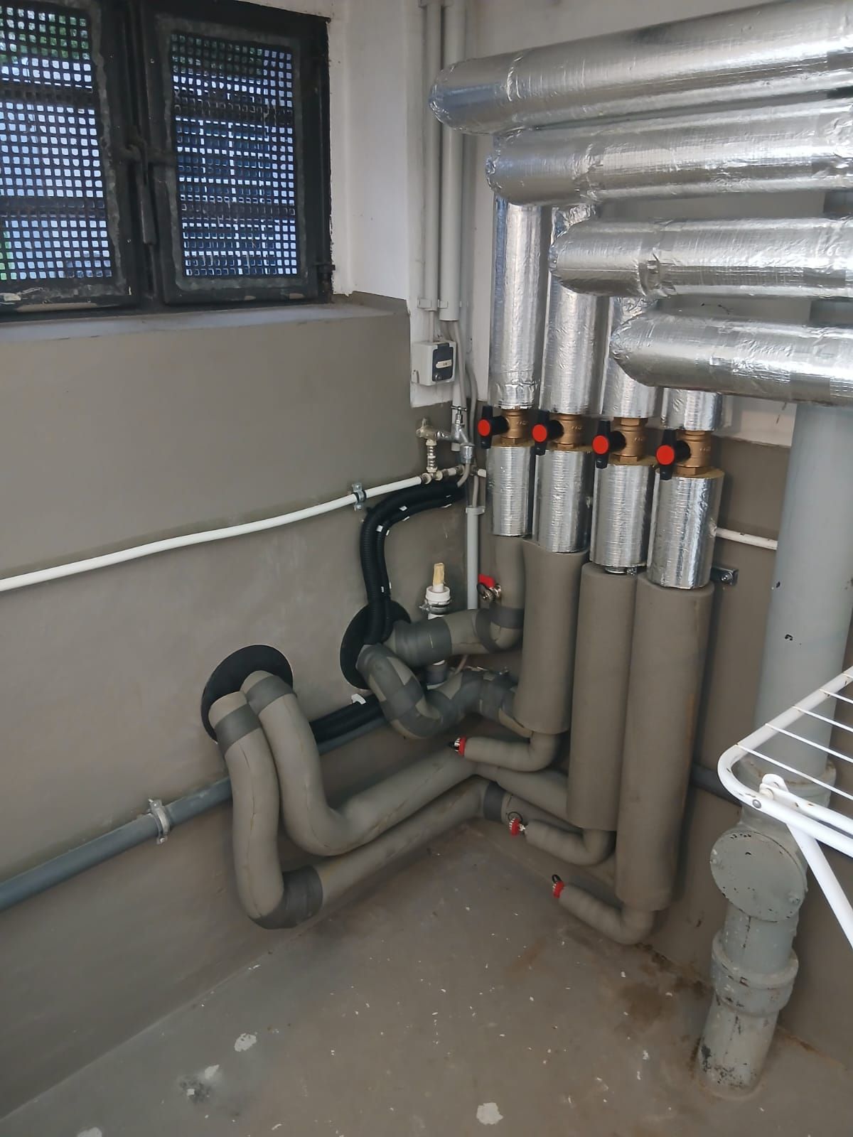 Verteilerbereich mit mehreren gedämmten Heizungsrohren und Absperrventilen im Keller.