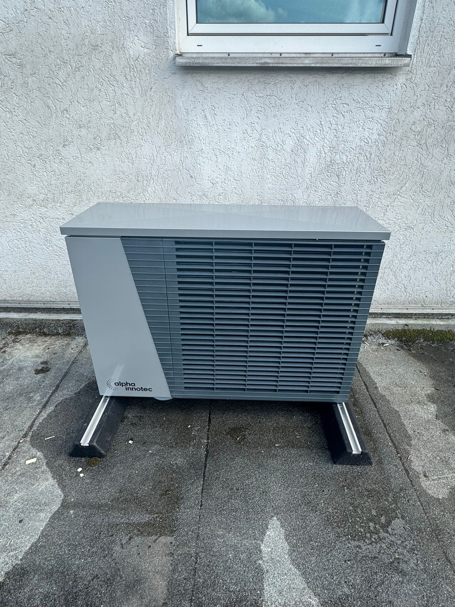Bosch-Außengerät auf Terrasse mit grauen Fliesen, vor roter Ziegelwand neben Glastür und Blumenbeet.