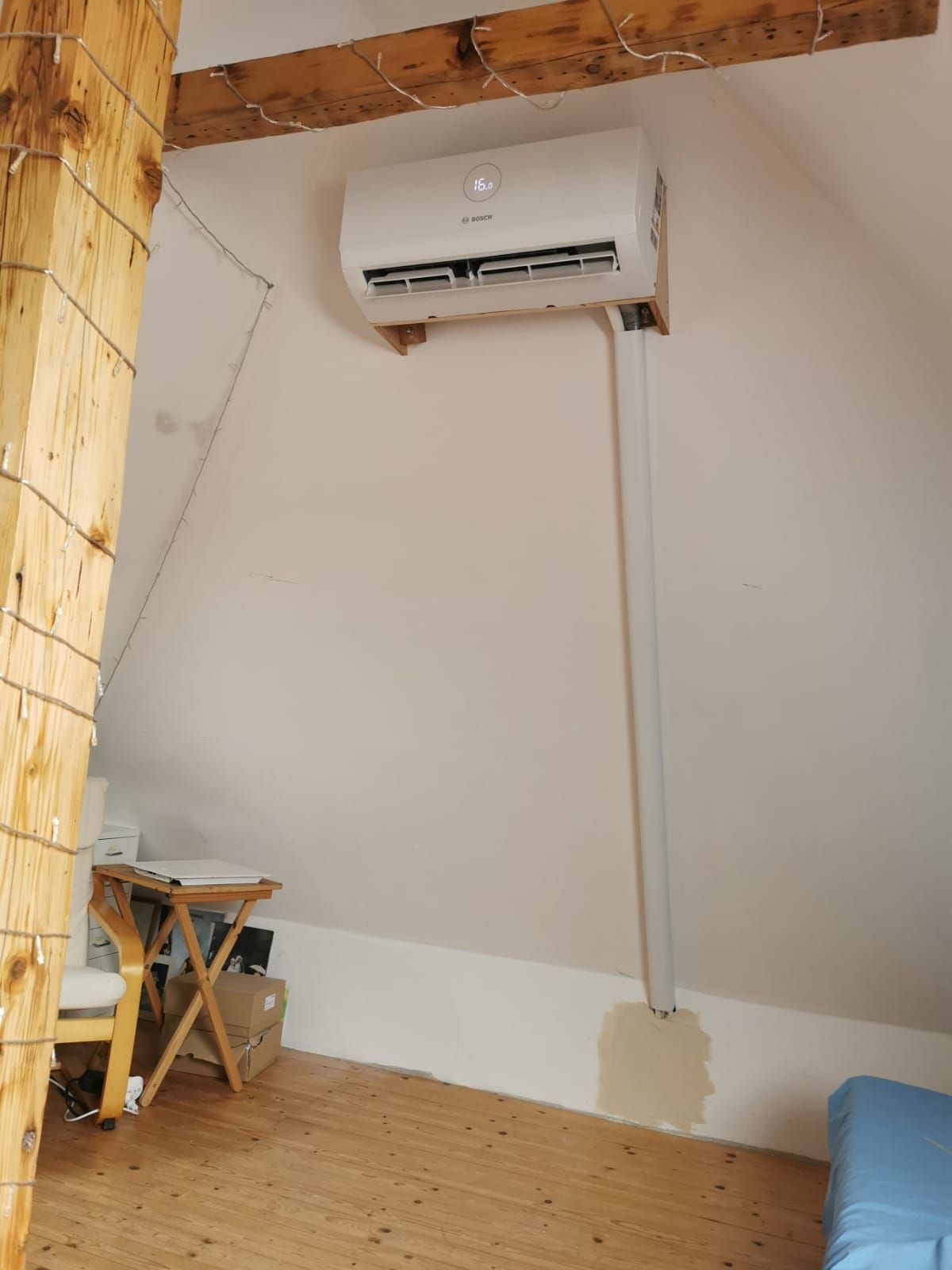 Innenaufnahme eines weißen Wandklimageräts über einer Fenstertür, Blick in einen gepflasterten Gartenbereich.