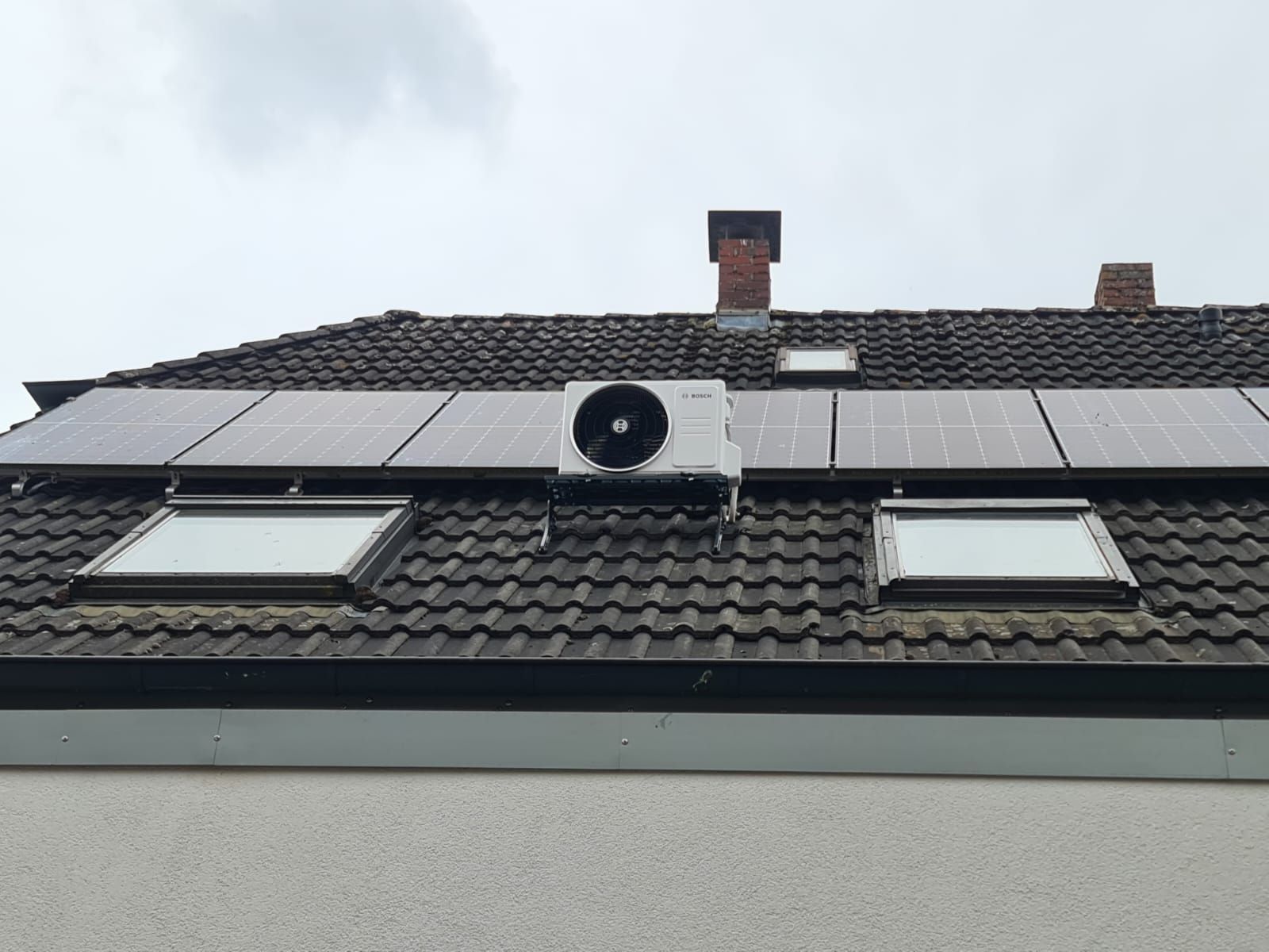 Bosch-Klimaanlage auf Hausdach montiert, eingebettet zwischen Photovoltaik-Modulen und Dachfenstern auf dunkler Ziegeldeckung.