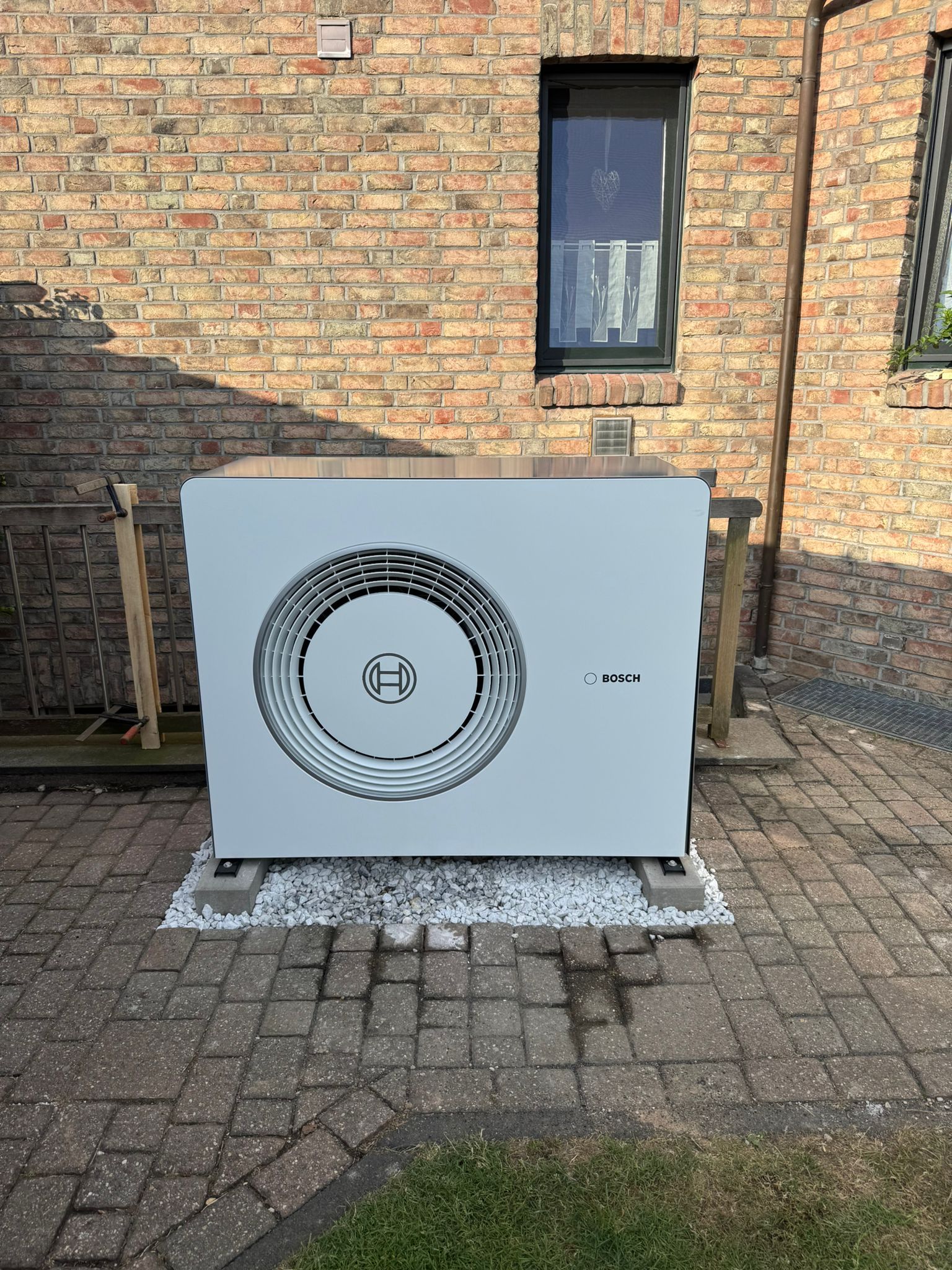 Bosch Wärmepumpen Außeneinheit auf Betonfundament vor Klinkerfassade neben Fenster.