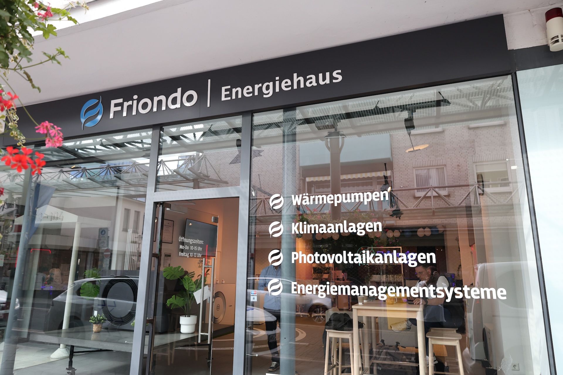 Beleuchtetes Logo der Friendo GmbH auf Holzlamellenwand mit Pflanzenrahmen – moderner und einladender Empfangsbereich.
