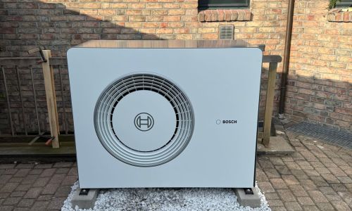 Bosch Wärmepumpen Außeneinheit auf Betonfundament vor Klinkerfassade neben Fenster.