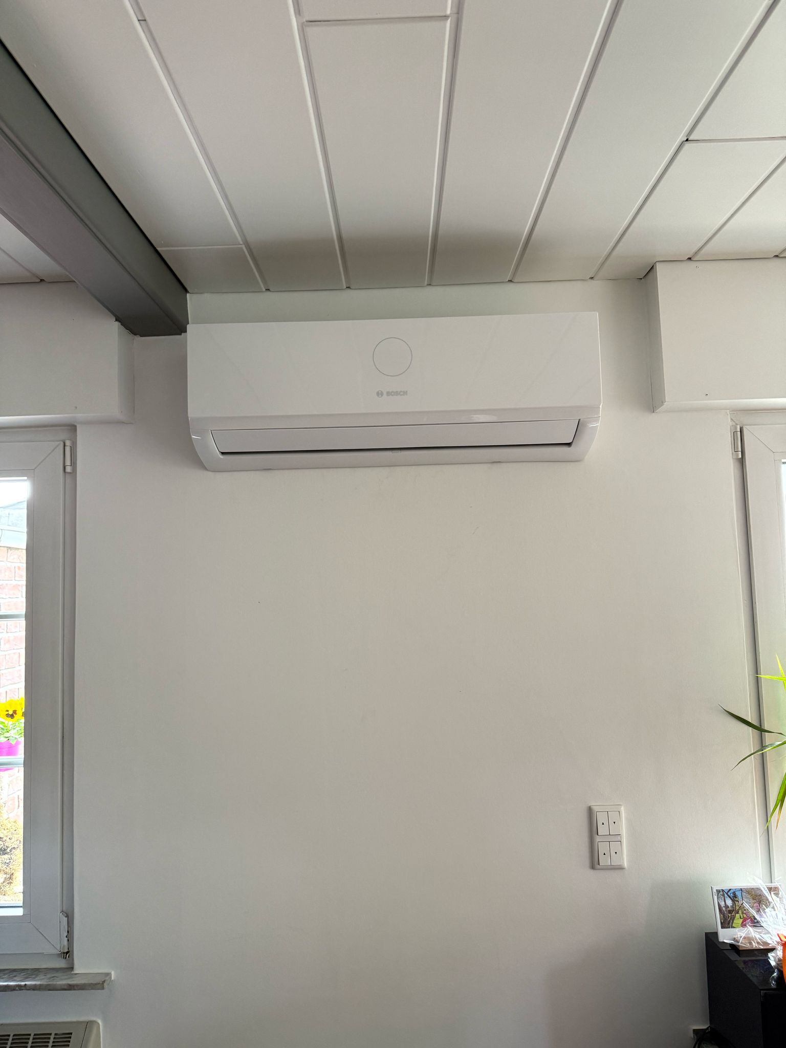 Bosch Klimainnengerät an weißer Wand, montiert nahe der Decke zwischen Fenster und Raumecke.