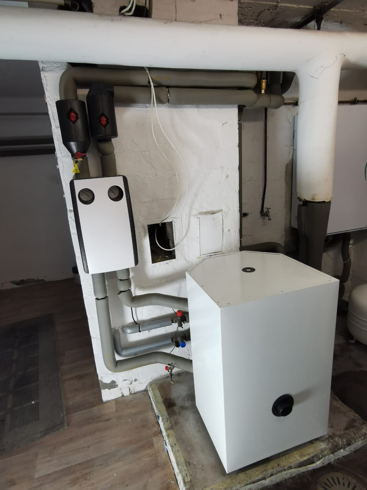 Heizungsinstallation mit Pufferspeicher, Verteilerbox und isolierten Leitungen im Technikraum.