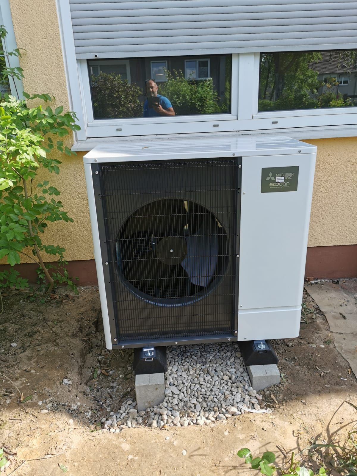 Frontansicht der Mitsubishi Ecodan Außeneinheit mit sichtbarem Ventilatorgitter vor Fassade.