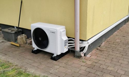 Innen montiertes Bosch Wandklimagerät unter Dachschräge, Leitungsführung sichtbar, Holzdecke und offener Raum.