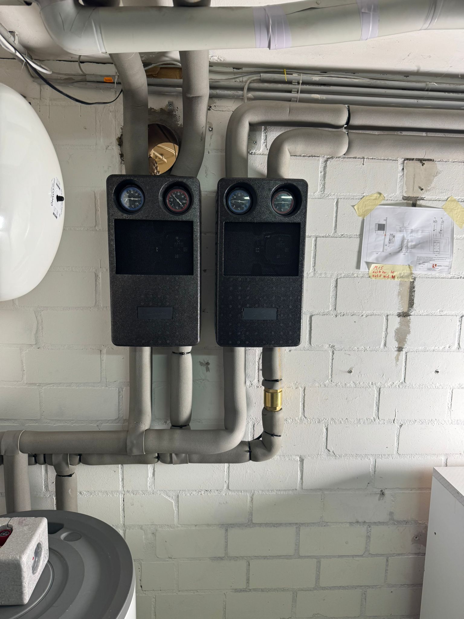 Zwei gedämmte Heizkreisgruppen mit Thermometern an Kellerwand montiert.