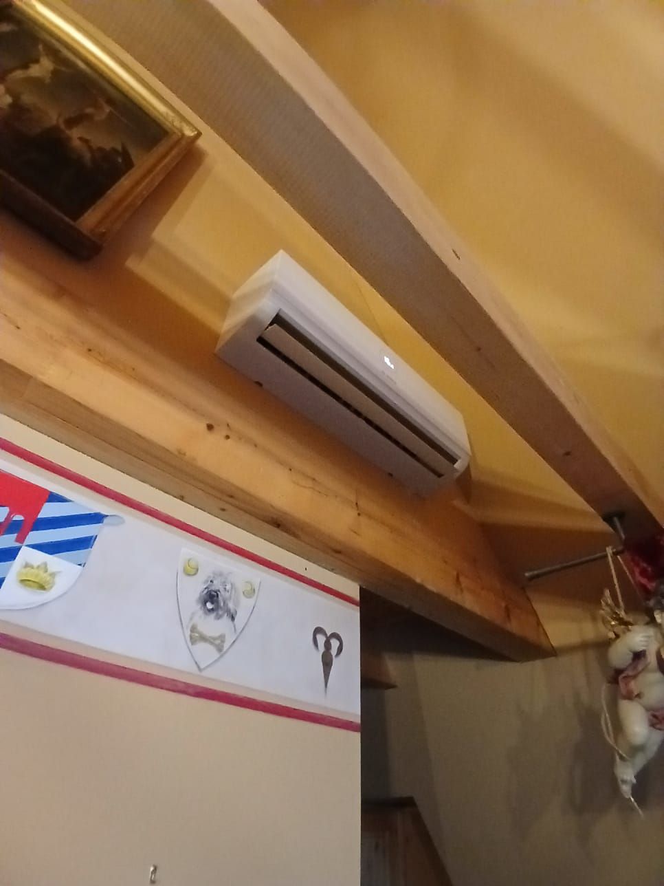 Bosch Klimainnengerät unter Holzbalkendecke montiert, positioniert über einer dekorierten Innenwand.